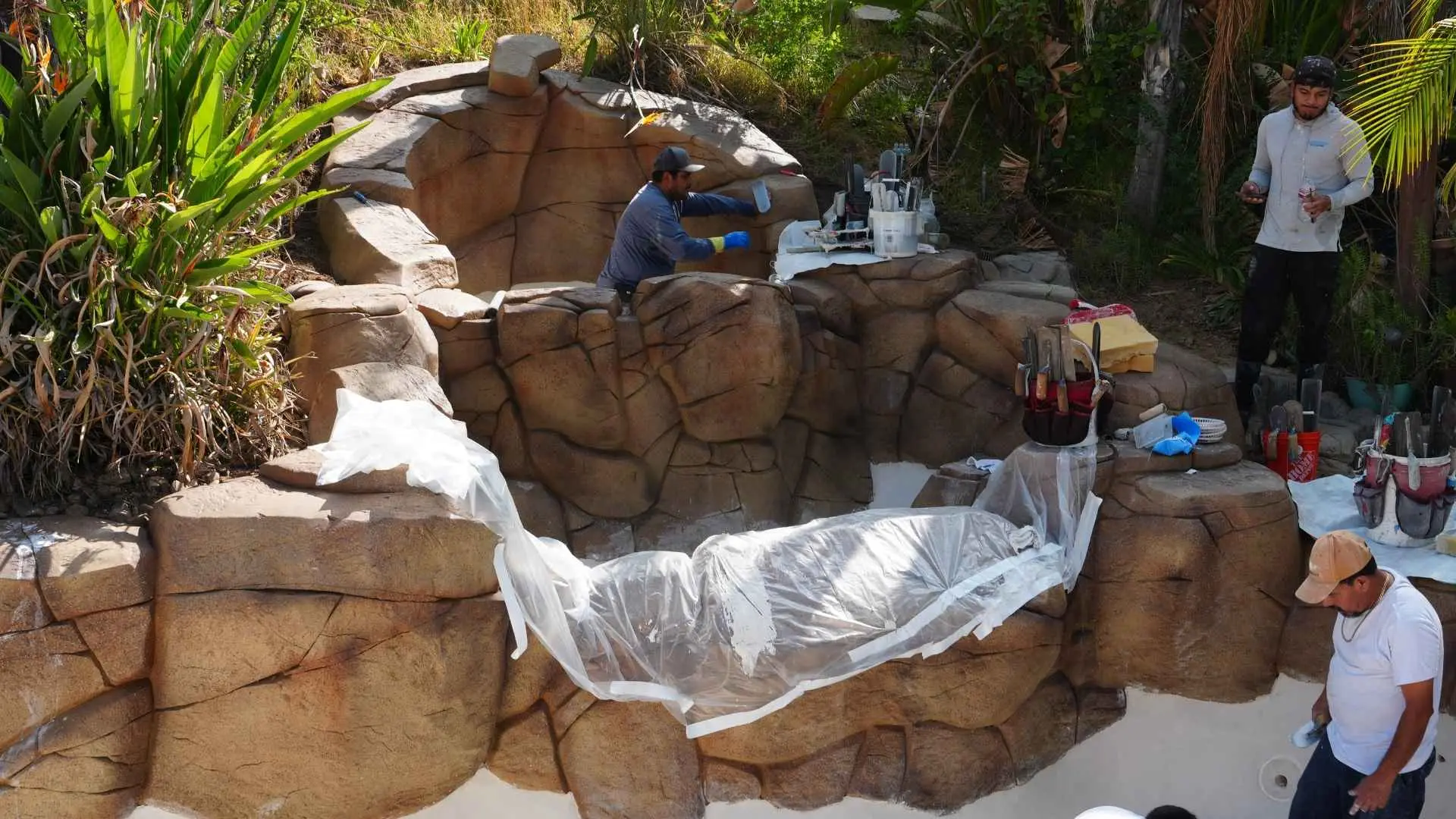 Aguas Pools crew hand-finishing an artificial rock waterfall beside a freshly plastered pool
