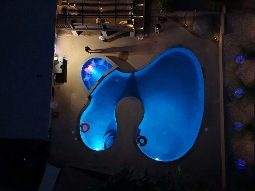 Freeform custom in-ground pool lit blue at night with attached raised spa