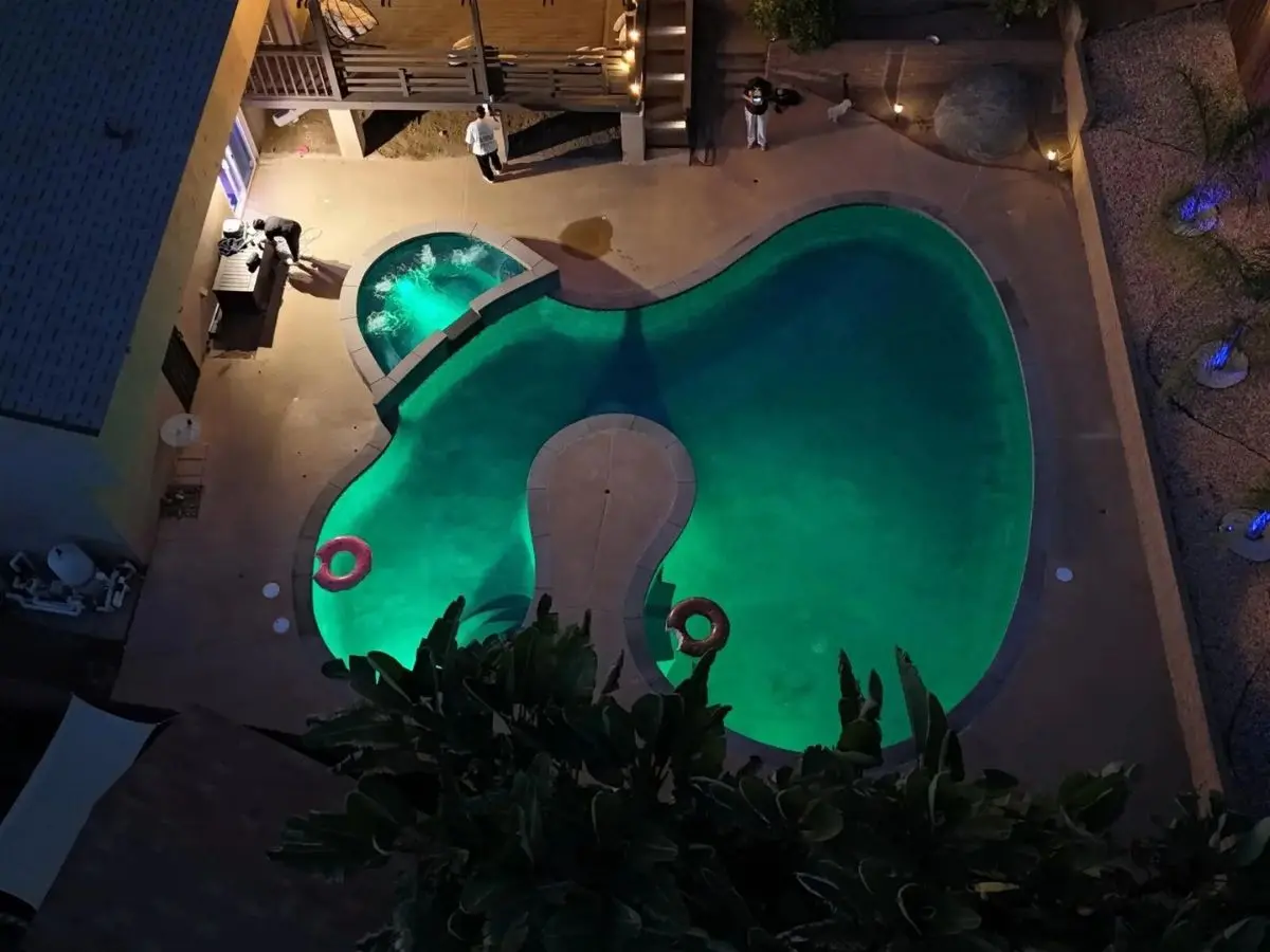 Pool and spa lit with green LED color lighting at night with landscape lights along the slope